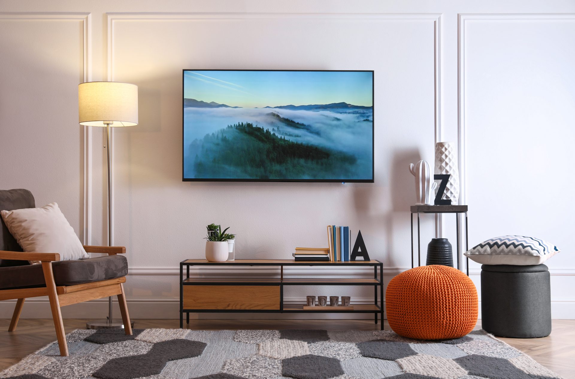 A lounge with a television mounted on a panelled white wall above a low timber media unit, with a floor lamp and an armchair