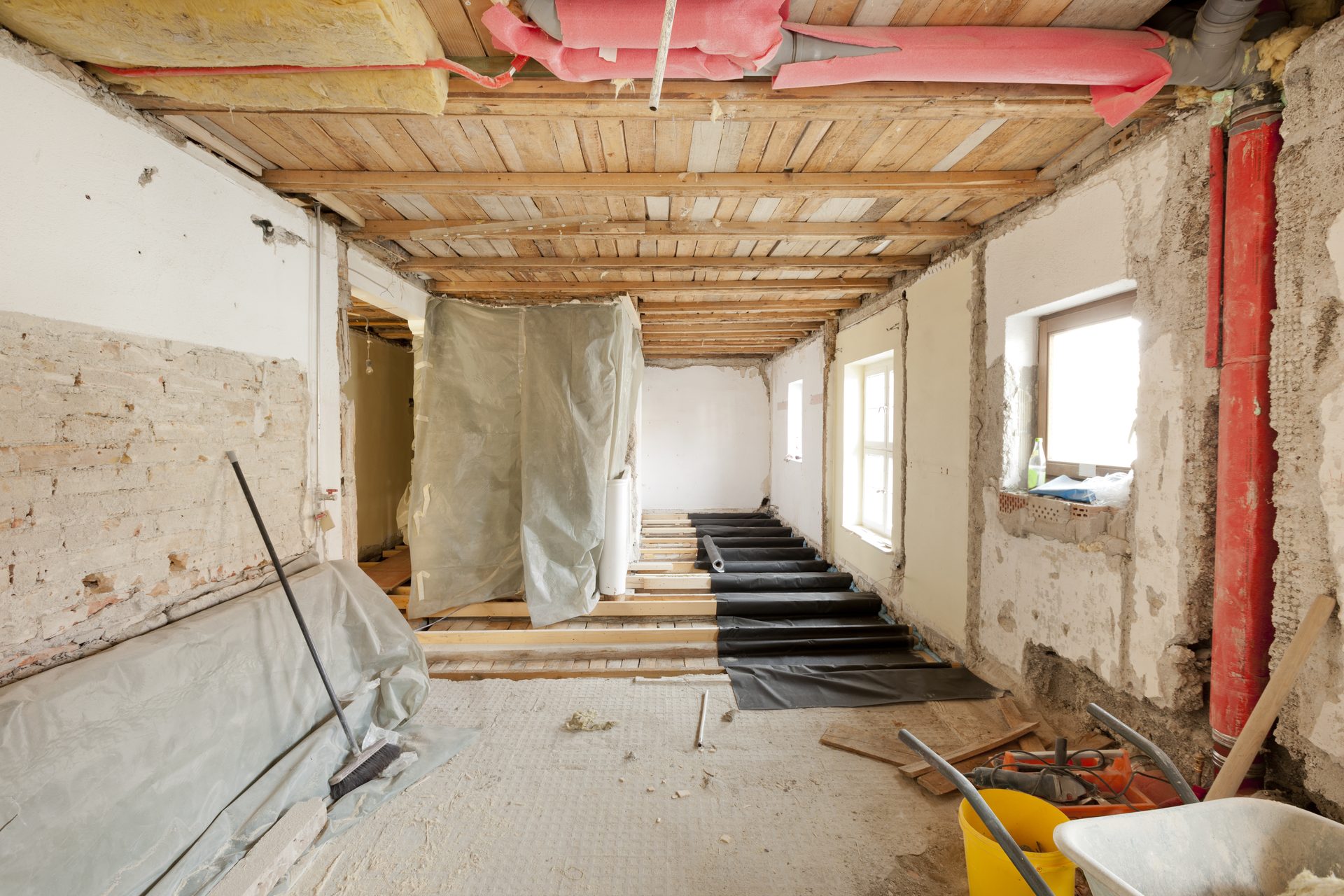 A room stripped back during a renovation, with the ceiling joists, floor framing and old plaster walls exposed and the floor covered in dust sheets